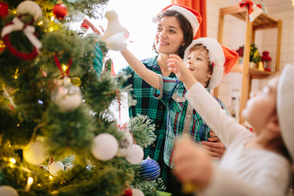クリスマスツリーとギフト付きの装飾されたクリスマスお祝いの部屋でクリスマスの冬の晴れた朝に幸せな家族のお母さん、息子、娘. - 写真・画像