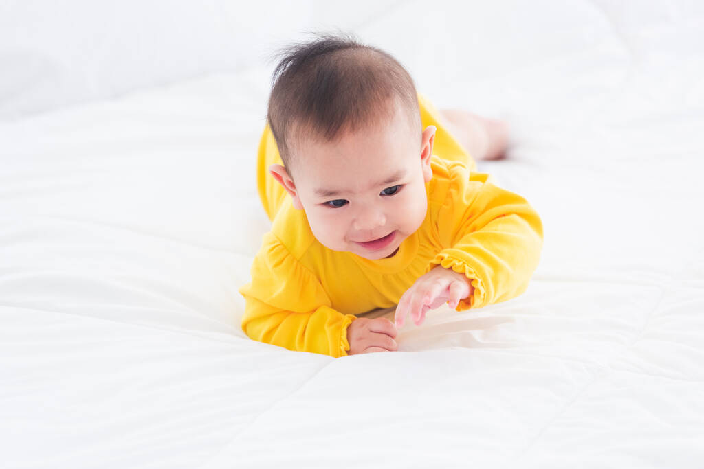 Porträt der schönen jungen asiatischen Neugeborenen Baby auf dem Bett zu Hause gestreckt, Happy Baby Smile trägt ein gelbes Hemd entspannt im Zimmer, Familienmorgen zu Hause - Foto, Bild