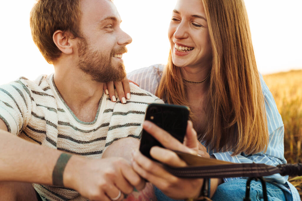 Immagine di una giovane coppia felice allegra amorevole che usa il telefono cellulare fuori sul campo mentre tiene il piombo - Foto, immagini