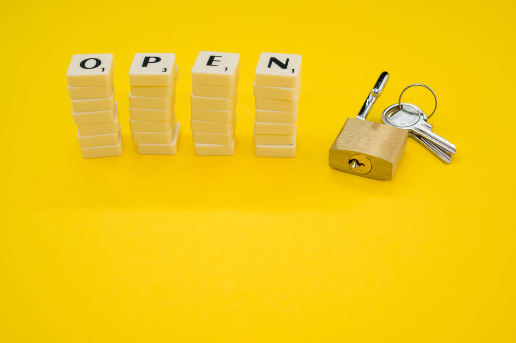 Neljä valkoista kirjainpinoa, jotka muodostavat sanan OPEN riippulukolla ja keltaisella taustalla olevilla avaimilla - Valokuva, kuva