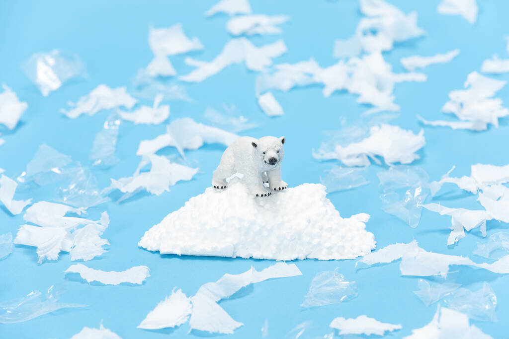 Gros plan d'un jouet d'ours polaire entouré de morceaux de plastique et de papier sur fond bleu - Photo, image