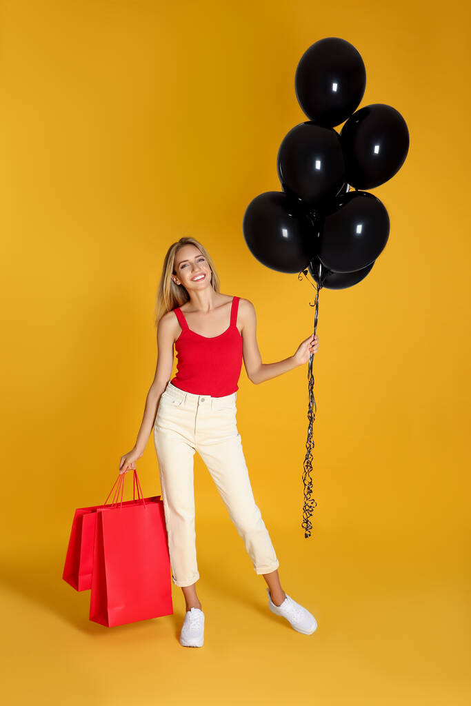 Happy young woman with balloons and shopping bags on yellow background. Black Friday Sale - Photo, Image
