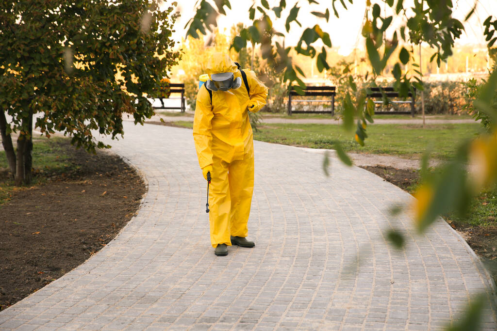 Henkilö hazmat puku desinfiointi katu jalkakäytävä sumutin. Pintakäsittely sepelvaltimoviruksen aiheuttaman pandemian aikana - Valokuva, kuva