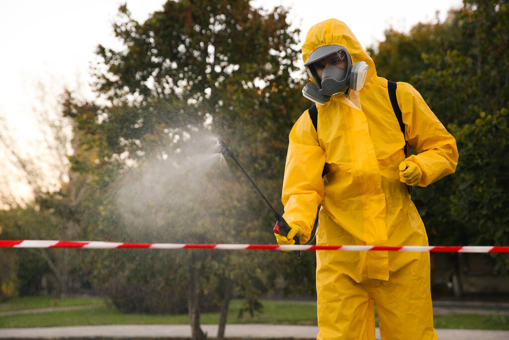 Persona en traje de materiales peligrosos desinfectando calle con rociador. Tratamiento superficial durante la pandemia de coronavirus - Foto, Imagen