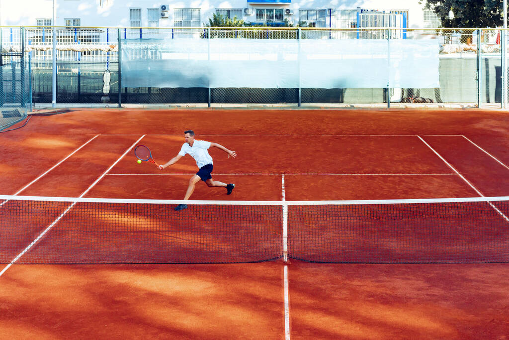 Homem joga tênis em campo de tênis de barro vista de longe - Foto, Imagem