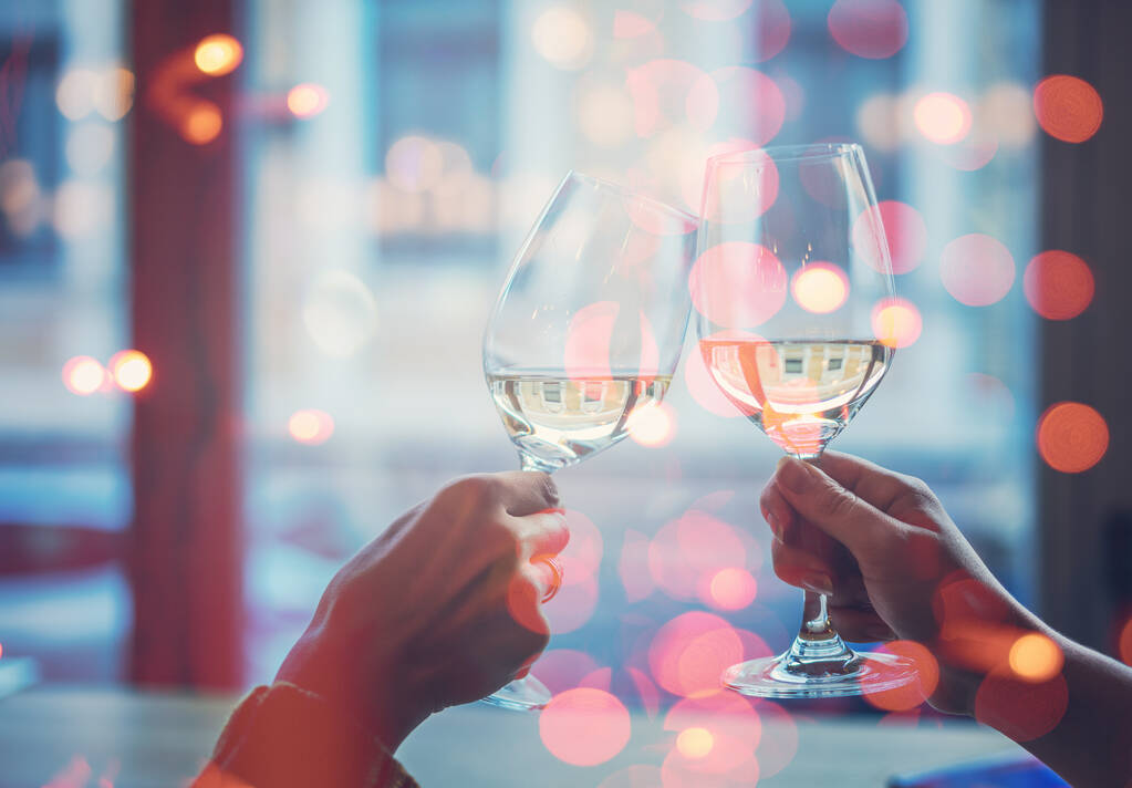 Dos manos con copas con vino blanco en el fondo de una ventana de primer plano, celebrando las fiestas - Foto, Imagen