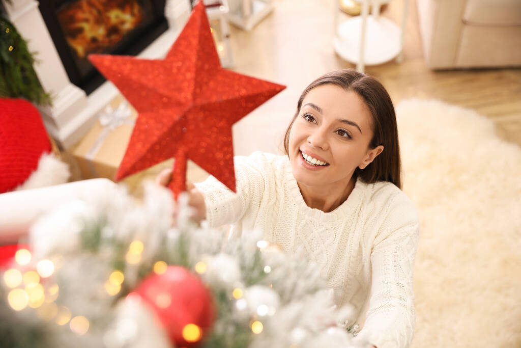 Frau schmückt Weihnachtsbaum mit Sternenhimmel im Zimmer - Foto, Bild
