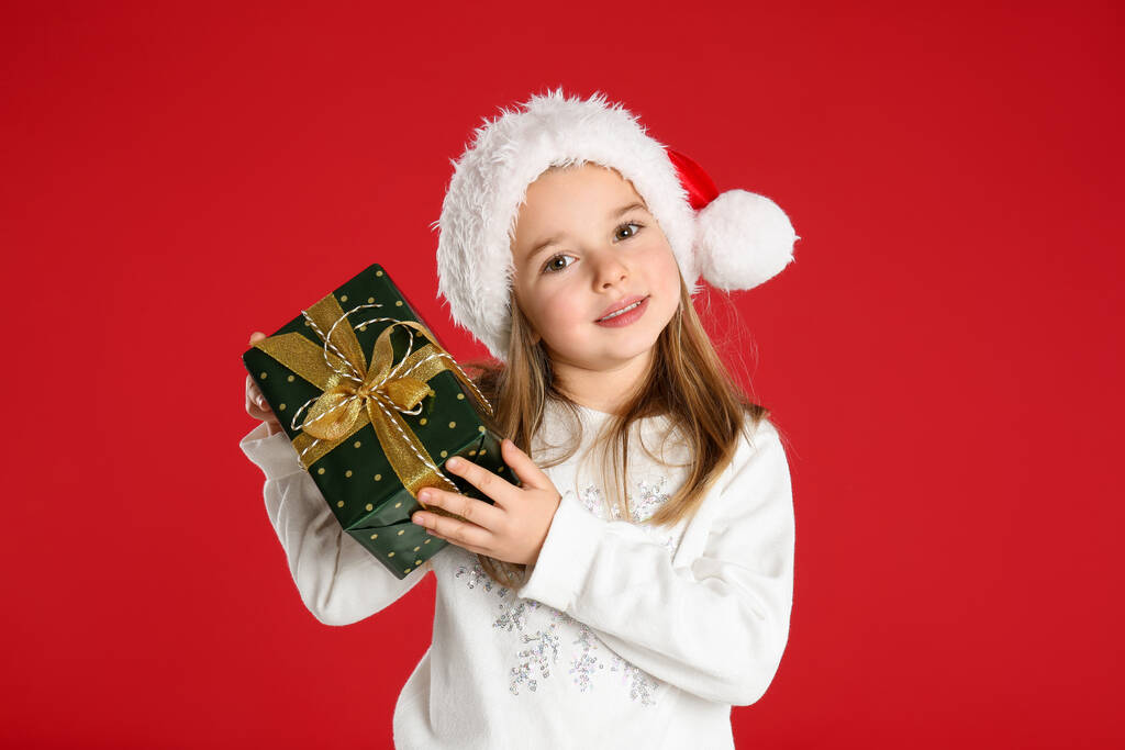 Lindo niño en sombrero de Santa con regalo de Navidad sobre fondo rojo - Foto, imagen