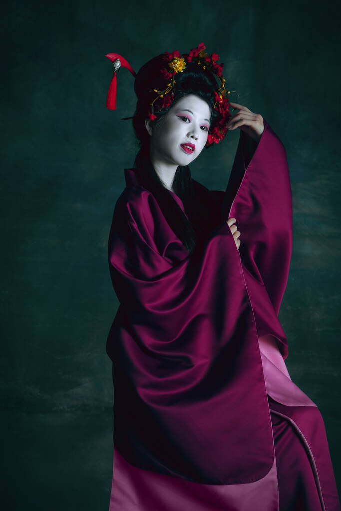 Fiatal japán nő, mint gésa, sötétzöld háttérrel. Retro stílus, a korszakok fogalmának összehasonlítása. - Fotó, kép