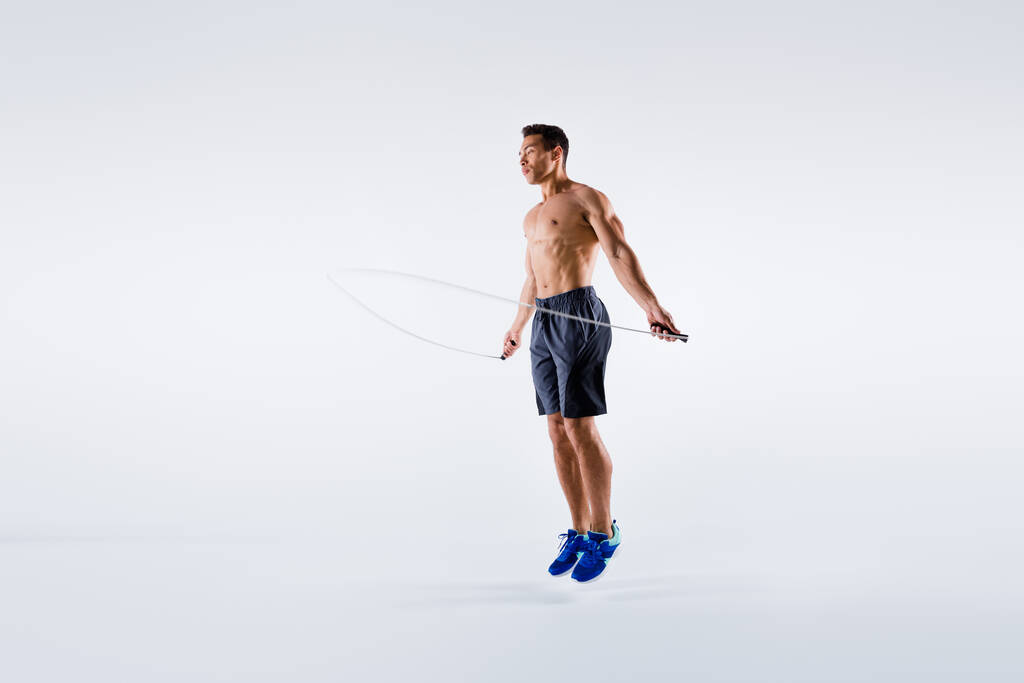 Фотографія повної довжини спортивного хлопця з використанням пропускаючої мотузки для тренування свого ідеального тіла ізольованого на білому тлі
 - Фото, зображення