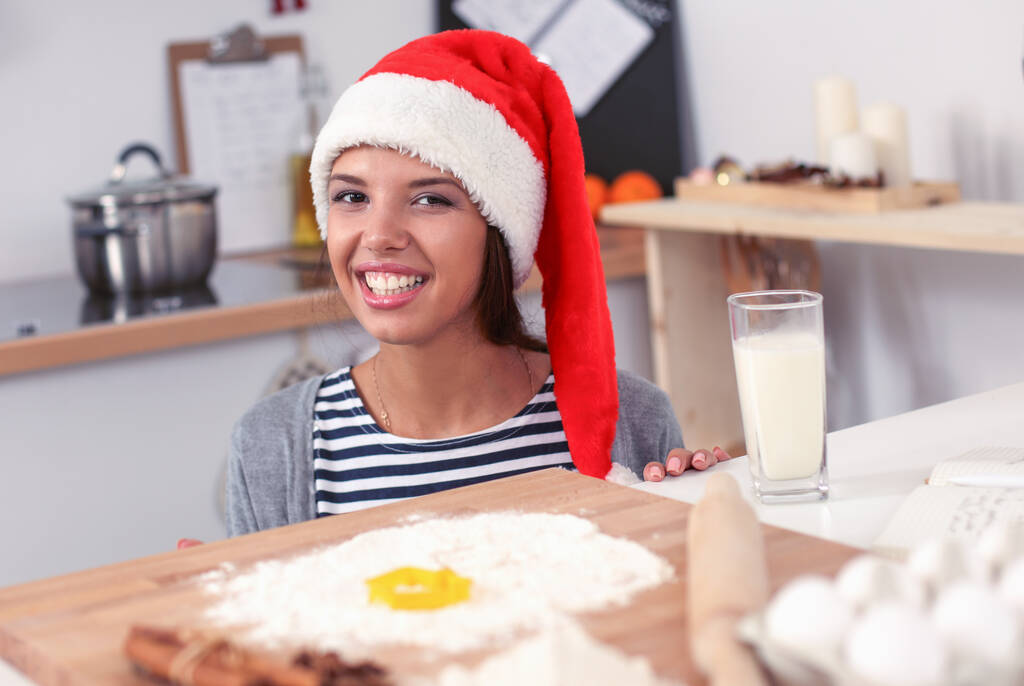 Femme au chapeau de Père Noël faire des biscuits de Noël dans la cuisine - Photo, image