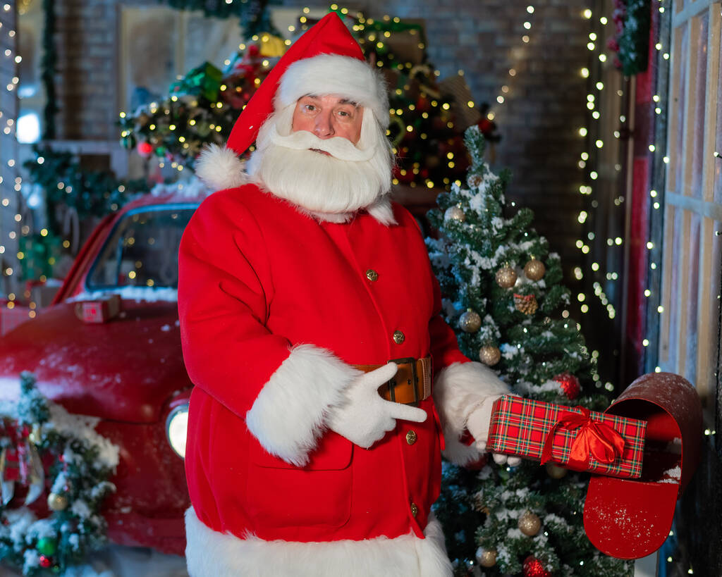 Der Weihnachtsmann verschickt ein Geschenk per Post. Ein als Weihnachtsmann verkleideter Mann legt einen geschmückten Kasten in einen Briefkasten - Foto, Bild