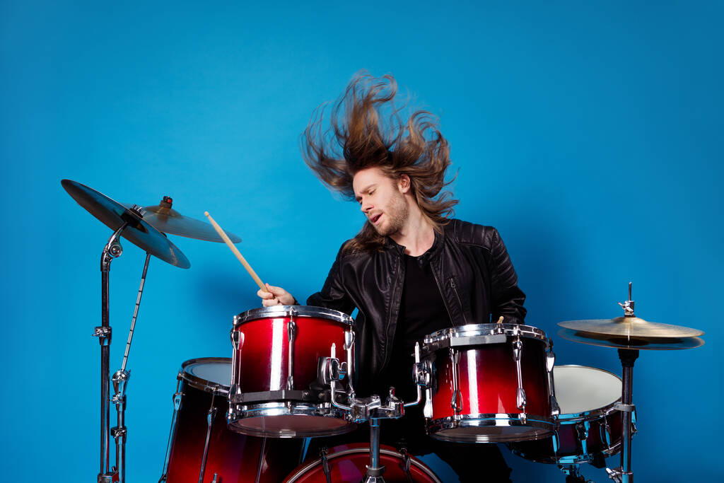 Portrét slavného umělce muž rocker hrát bicí složení na pódiu koncertní turné držet stehno nosit koženou bundu jeho vlasy vzduch létat izolované přes jasný lesk barvy pozadí - Fotografie, Obrázek