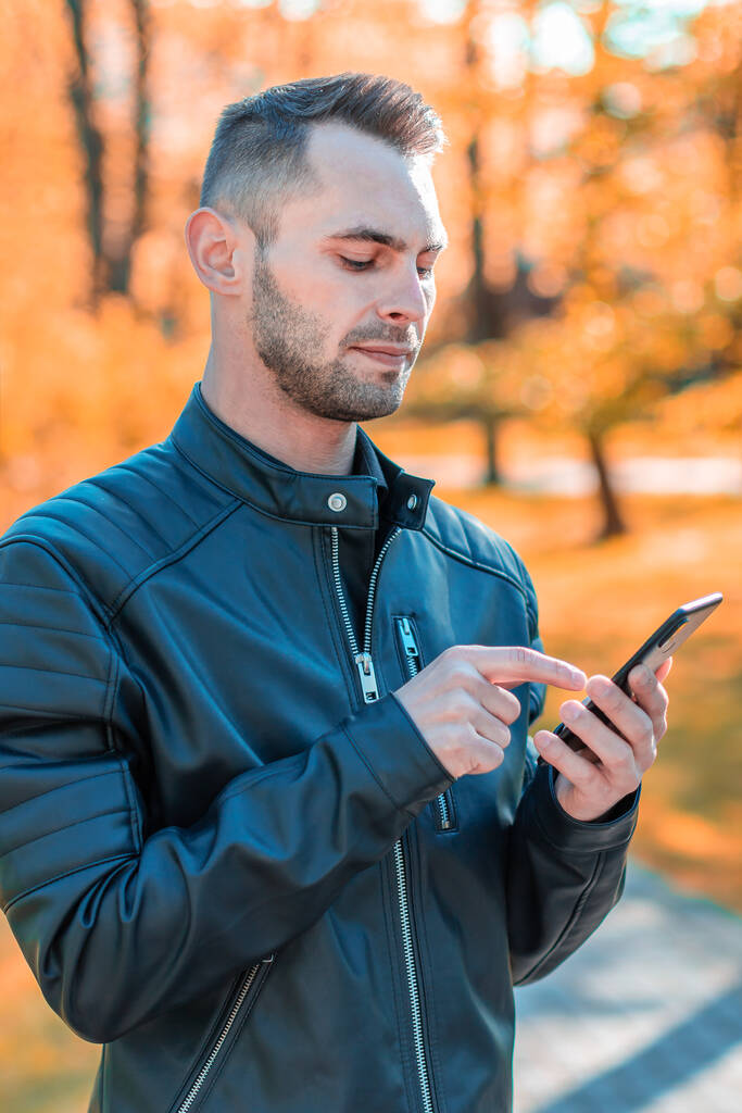 Chico guapo usando Smartphone en Autumn Park - Foto, imagen