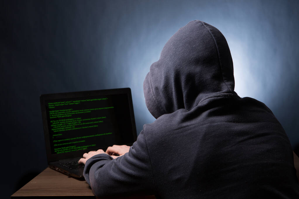 Hacker in cappuccio con computer portatile che avvia l'attacco informatico. Vista dal retro. - Foto, immagini