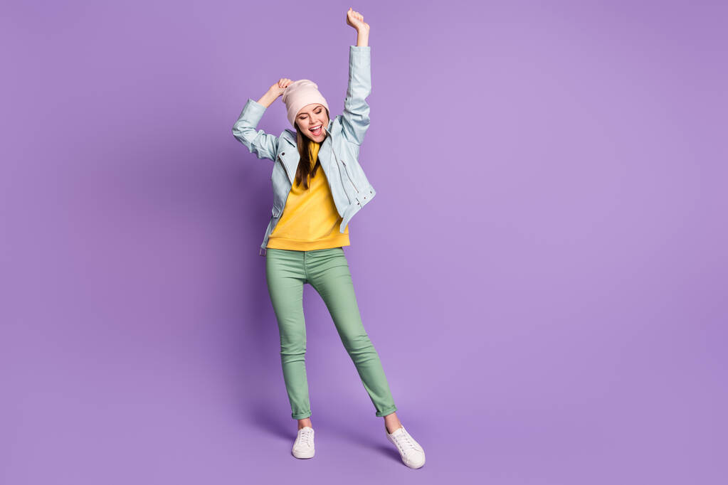 Full length photo of funny attractive lady good mood raise arms up excited cheerful wear casual hat modern blue jacket green pants sneakers isolated purple color background - Photo, Image