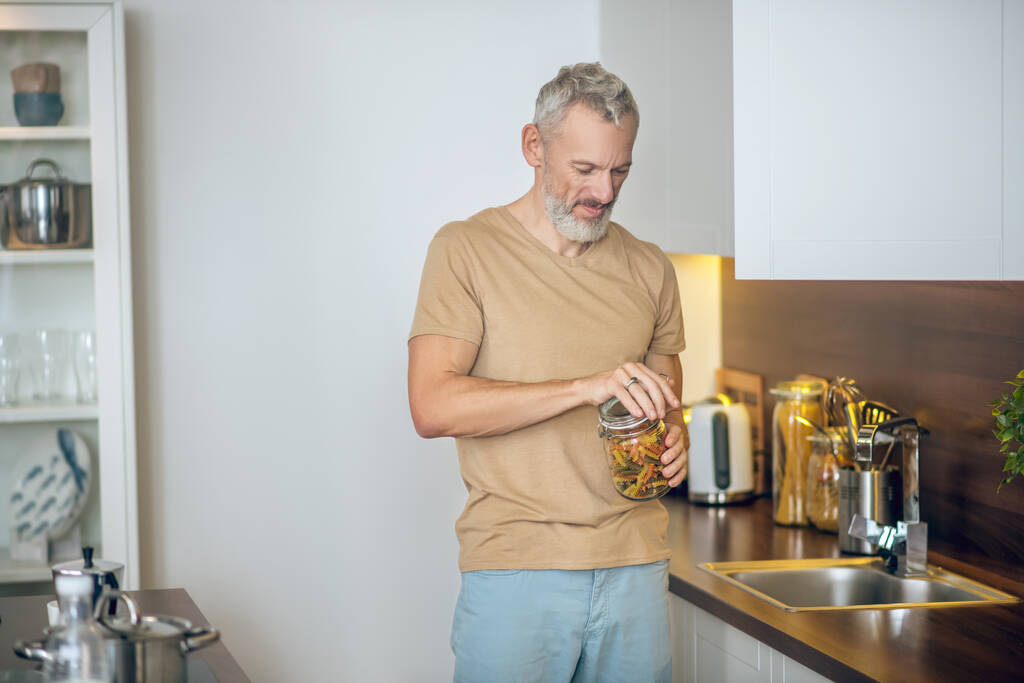 Hombre barbudo maduro en camiseta beige en la cocina en casa - Foto, imagen