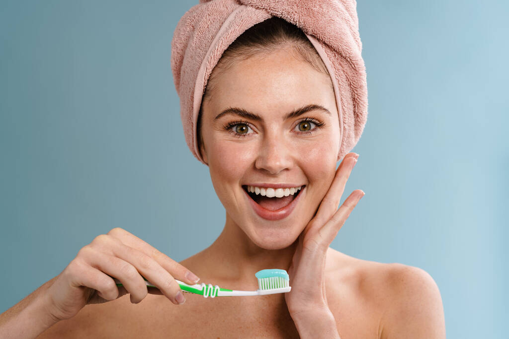 Bez koszuli szczęśliwa dziewczyna w ręczniku gospodarstwa szczoteczka do zębów z pastą izolowane na niebieskim tle - Zdjęcie, obraz