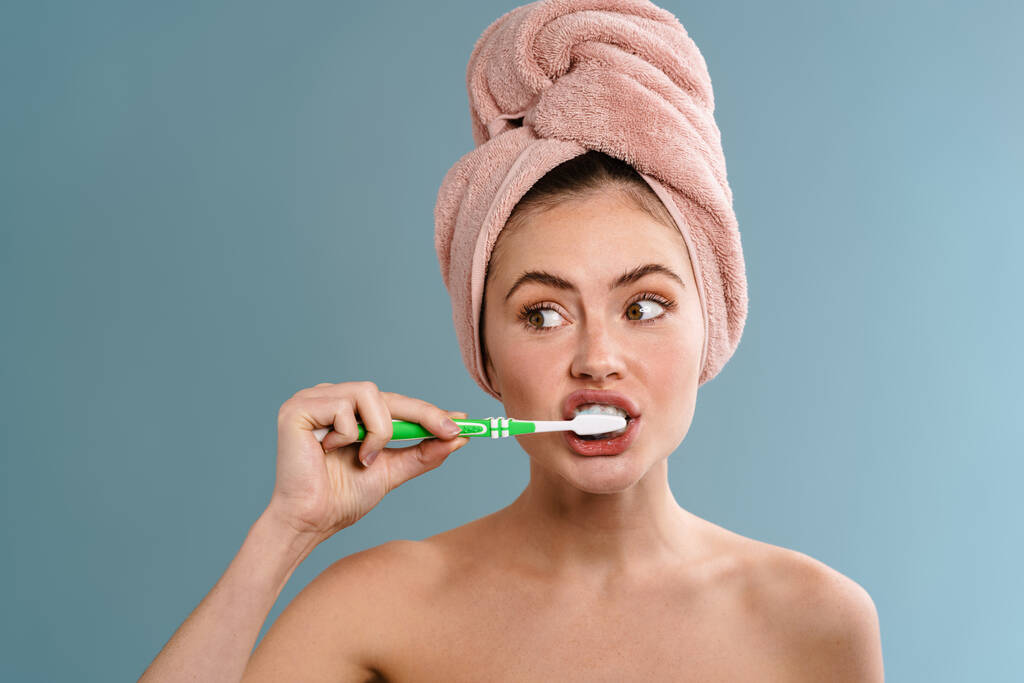 Bild einer jungen schönen Frau in Handtuch Zähne putzen isoliert über blaue Wand Hintergrund - Foto, Bild
