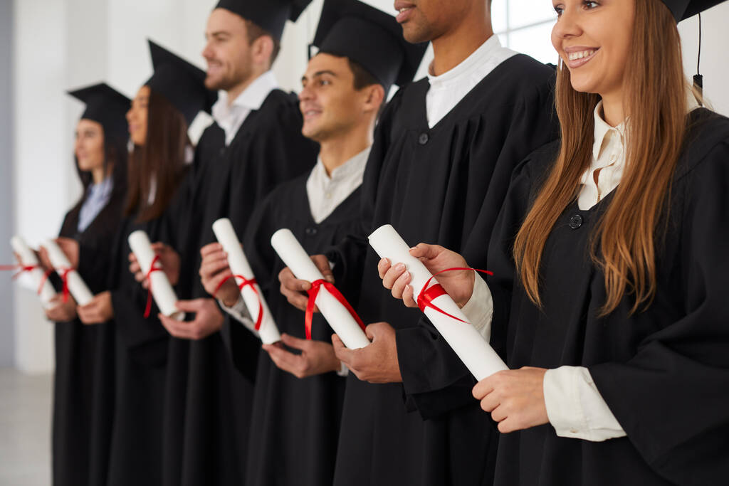 Группа мультиэтнических людей, стоящих в ряд и держащих в руках свитки дипломов. - Фото, изображение