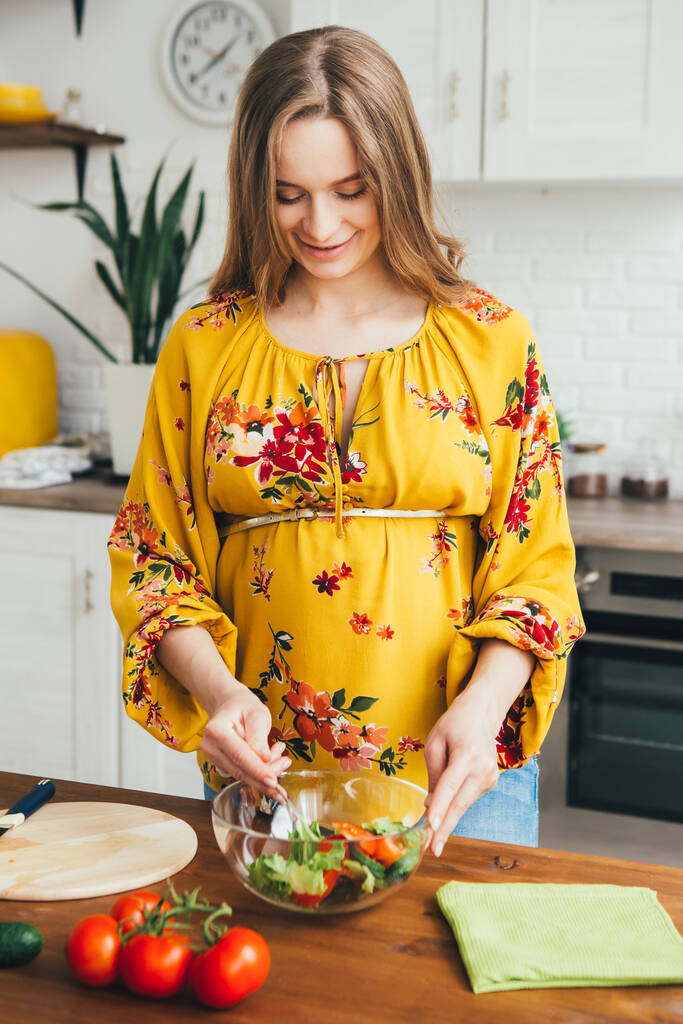 Young cute pregnant girl preparing vegetable salad in the kitchen. The concept of healthy eating. Toning. - Photo, Image