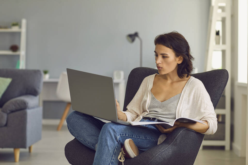 Nainen istuu kannettavan tietokoneen ja muistikirjan kanssa ja juttelee jonkun kanssa videokallin aikana - Valokuva, kuva
