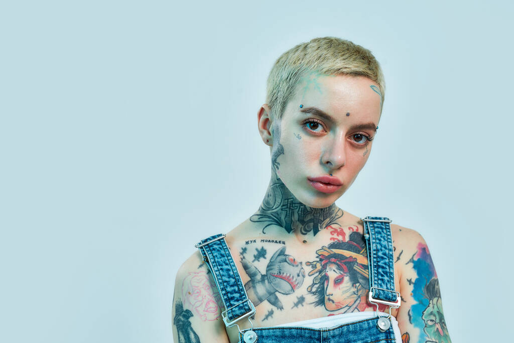 Primo piano di una donna tatuata bianca con piercing guardando in una macchina fotografica con la testa leggermente inclinata - Foto, immagini