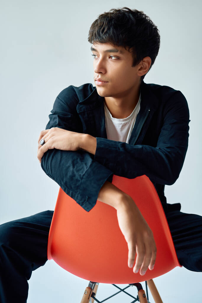 Stilvolle schöne junge Mann posiert im Studio sitzt auf einem Stuhl auf weißem Hintergrund - Foto, Bild