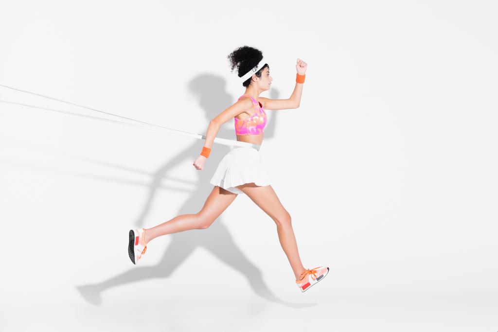 вид сбоку женщины, выполняющей упражнения с лентой сопротивления на белом - Фото, изображение