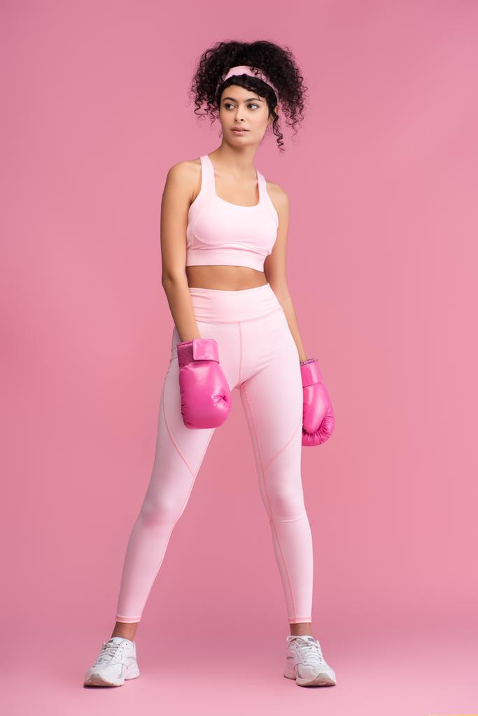повна довжина кучерявої молодої жінки в спортивному одязі та боксерських рукавичках на рожевому
  - Фото, зображення