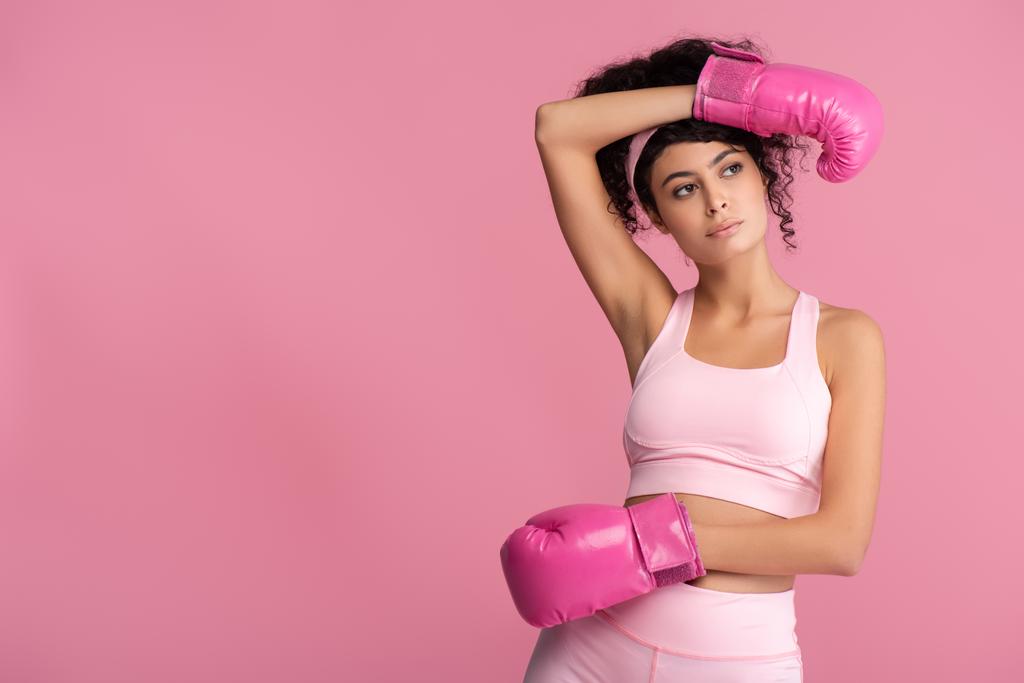 bruna e riccia donna in abbigliamento sportivo e guanti da boxe isolati su rosa  - Foto, immagini