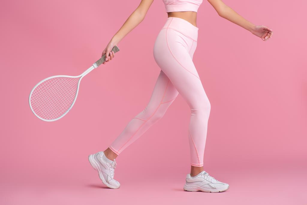 vista ritagliata di giovane donna in abbigliamento sportivo con racchetta mentre gioca a tennis isolato su rosa  - Foto, immagini