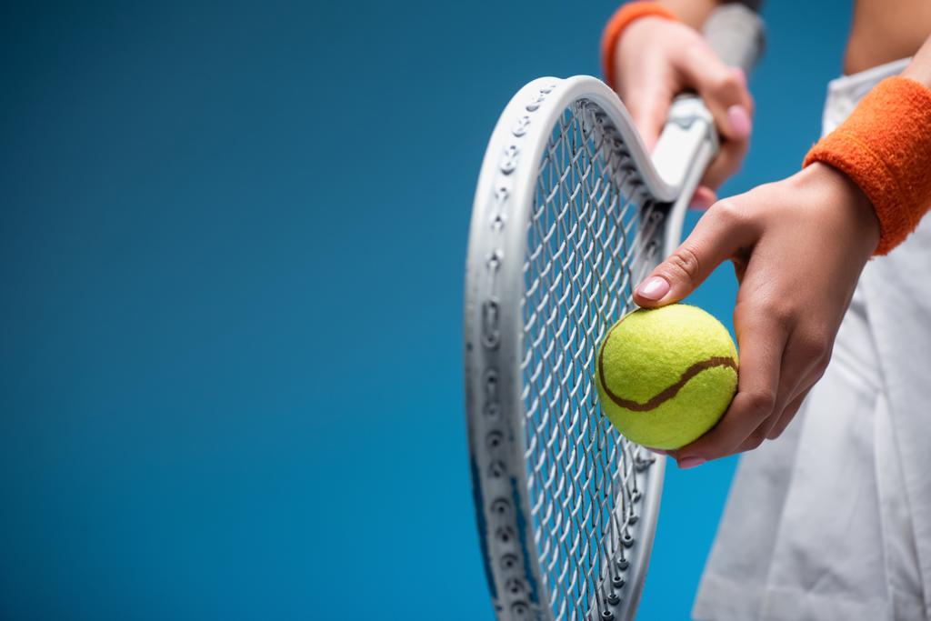 partial view of sportive young woman holding tennis racket and ball while playing on blue - Photo, Image