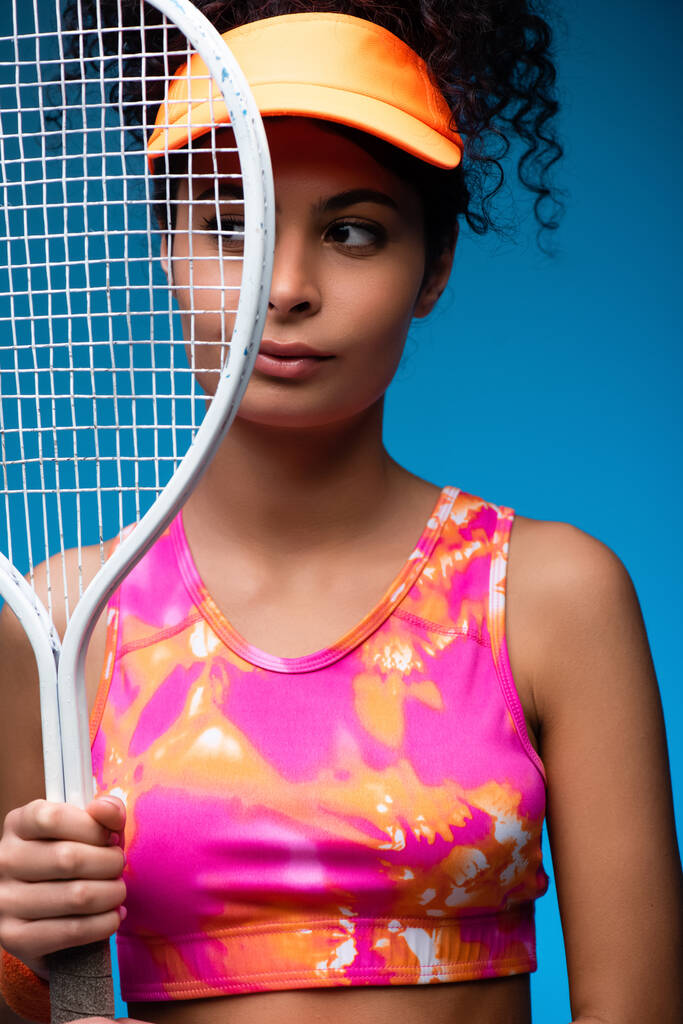 σπορ νεαρή γυναίκα κοιτάζει μακριά, ενώ κρατώντας ρακέτα τένις στο μπλε - Φωτογραφία, εικόνα