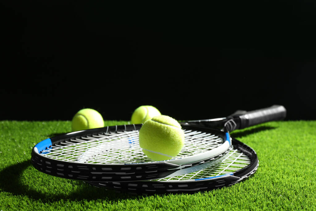Tennis rackets and balls on green grass against dark background. Space for text - Photo, Image