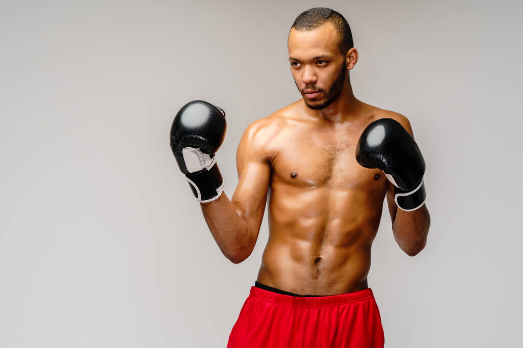 Confiado joven boxeador africano en guantes de boxeo de pie sobre fondo gris claro - Foto, imagen