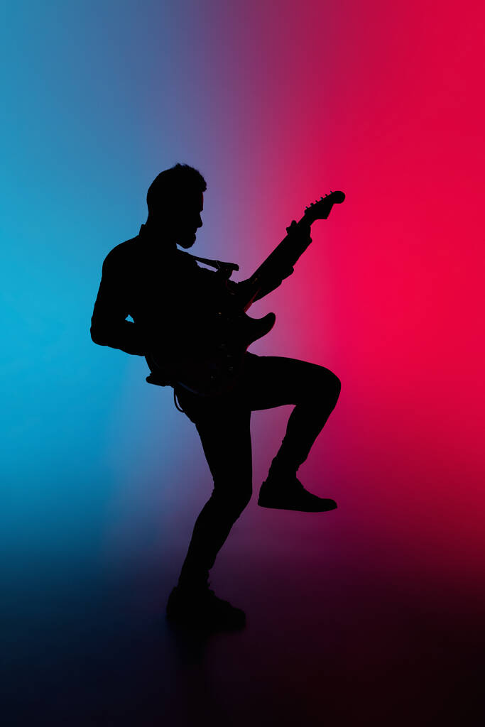 Silhouette eines jungen kaukasischen männlichen Gitarristen isoliert auf blau-rosa Farbverlauf Studiohintergrund in Neonlicht - Foto, Bild