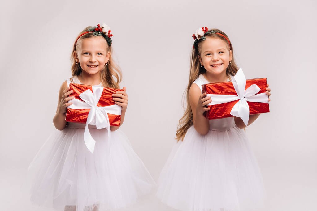 two little girls in white dresses with Christmas gifts on a white background smile. - Photo, Image