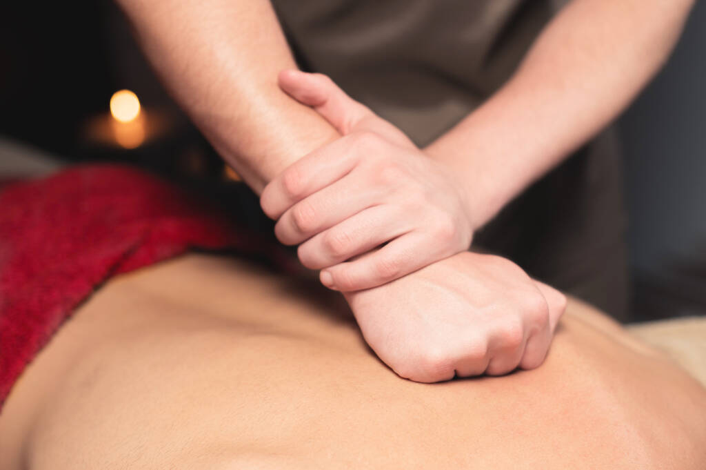 Масаж спини. Чоловічий масажист робить масаж спини чоловічому клієнту в темній кімнаті спа-салону
 - Фото, зображення