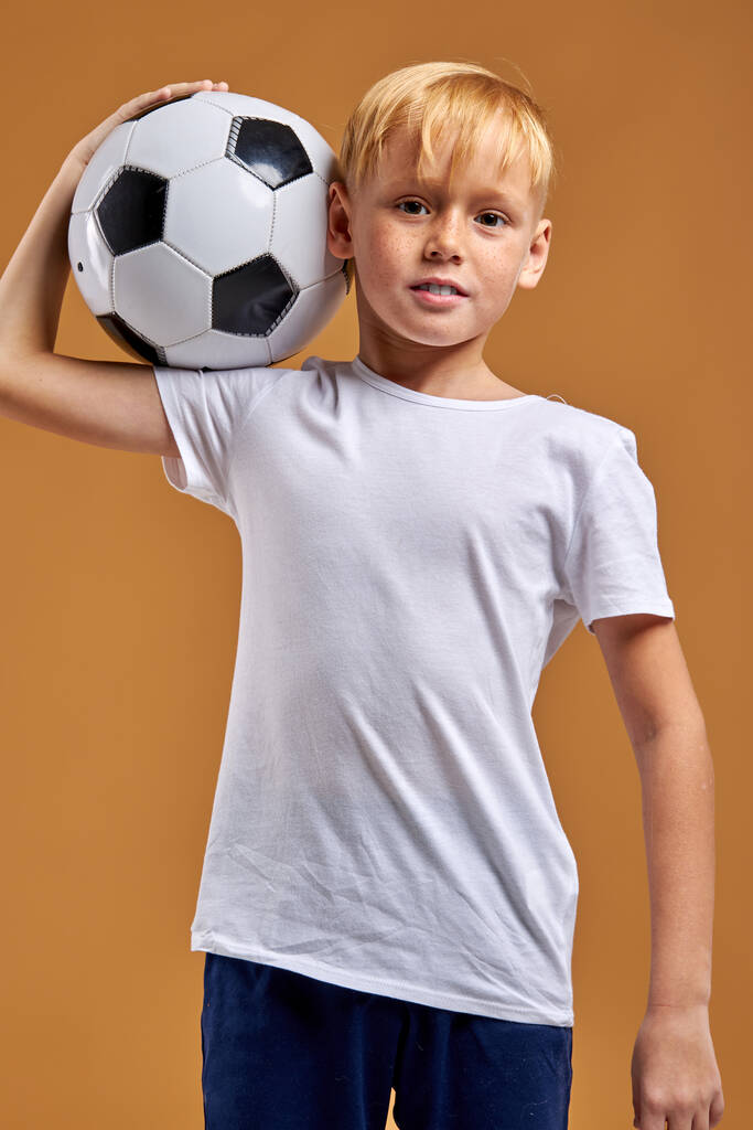 молодий футболіст хлопчик з м'ячем на плечах позує
 - Фото, зображення