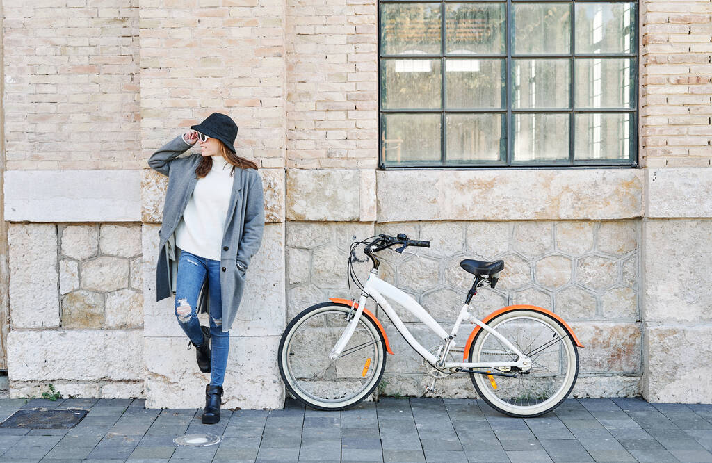 Un retrato joven bonita chica caucásica en ropa casual, con una bicicleta para un paseo, hablando por teléfono - Foto, imagen