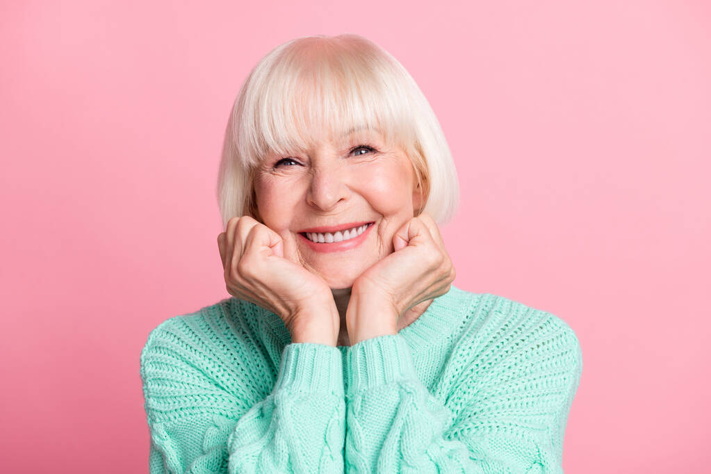 Foto portret van charmante senior vrouw in teal trui blond haar glimlachen aanraken wangen geïsoleerd op pastel roze kleur achtergrond - Foto, afbeelding