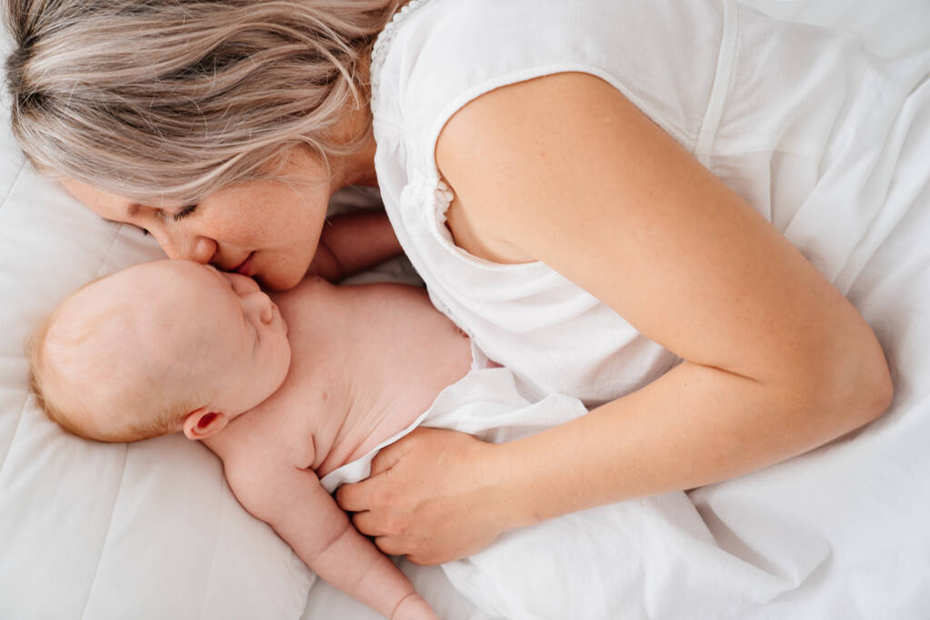 mom is mom is lying down with a baby in a white bed after feeding breast milk.  - Photo, Image