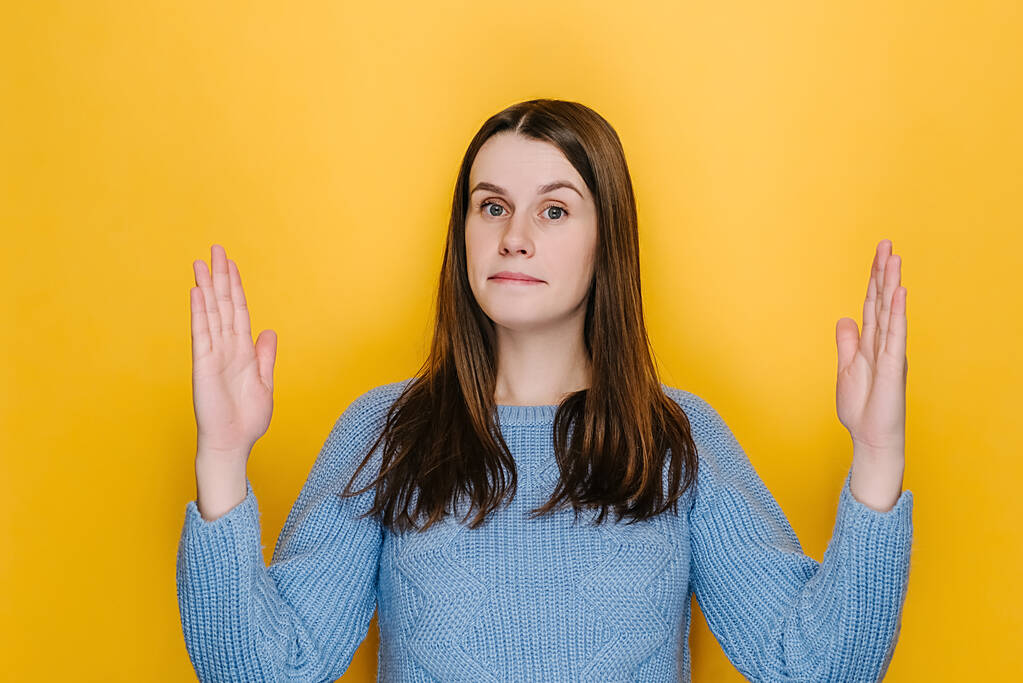Surprised young woman isolated on yellow studio background showing big size gesture with hands, attractive amazed female, impressed brunette girl demonstrate something wide, wears blue sweater - Photo, Image