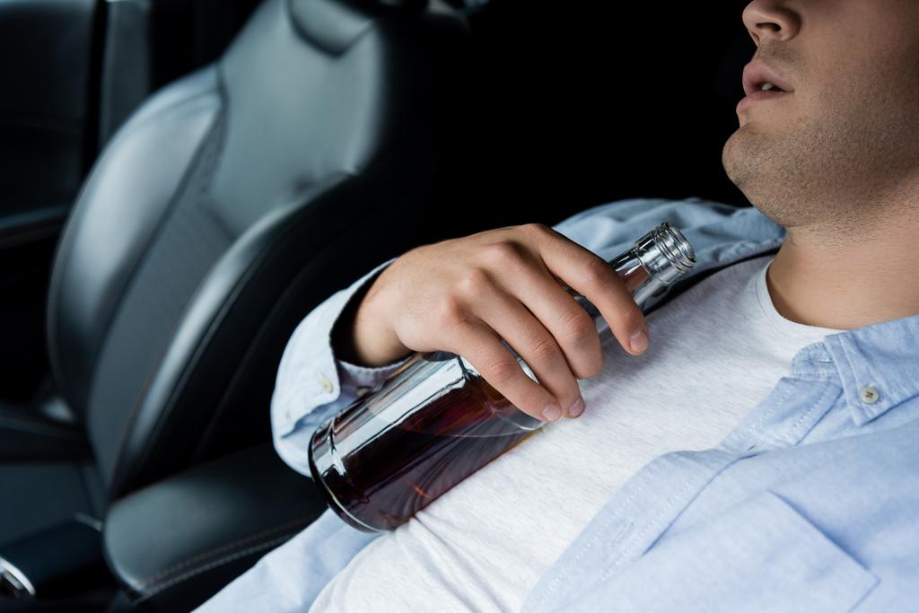 vista parcial del hombre borracho durmiendo con botella de alcohol en el asiento del conductor en el coche - Foto, Imagen