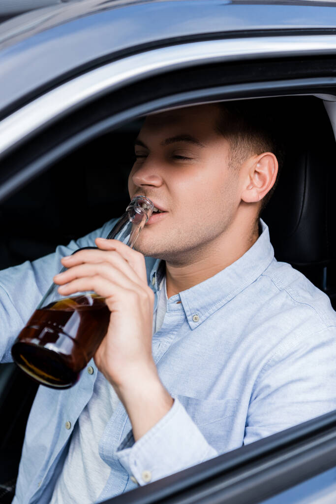 joven bebiendo whisky mientras conduce el coche en primer plano borroso - Foto, imagen