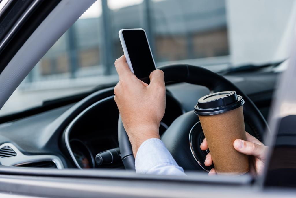 częściowy widok człowieka trzymającego kawę na wynos i rozmawiającego na smartfonie w samochodzie na niewyraźnym pierwszym planie - Zdjęcie, obraz