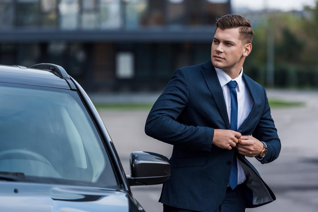 empresário abotoando blazer perto do carro, foreground borrado - Foto, Imagem