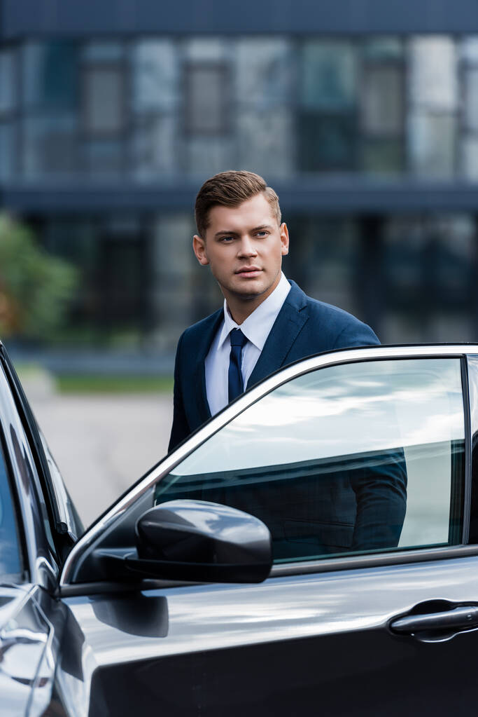 若いビジネスマンがドアを開けて車の近くに立っている - 写真・画像