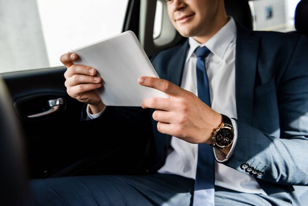 Обрезанный вид цифрового планшета в руках бизнесмена на размытом фоне в автомобиле - Фото, изображение